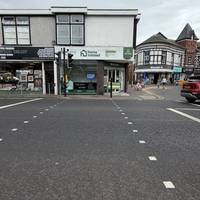Use the pelican crossing to cross over Grange Road towards the shops.