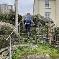With the sign behind you, turn right and walk along the lane until you reach the steps on the left. Head up them and onto the footpath.