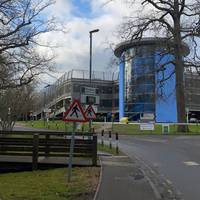 There is a blue building ahead of you, as well as staff parking. Continue in this direction.