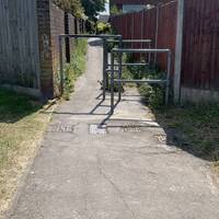 Continue to the end of the green space. Go through the metal barriers and head along the alleyway between the houses.