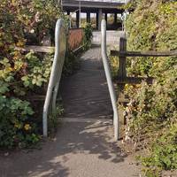 At the end of the path go through a squeeze stile and across a footbridge to emerge on a slip road near a roundabout.