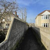 Turn left onto a tarmac pathway between houses.