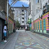 Cross the bus access lane via the pedestrian crossing and drop kerbs, then head through the colourful Rosebank Villas path.