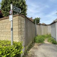 Turn left onto a narrow footpath by a fingerpost sign between a wooden fence and an electricity building.