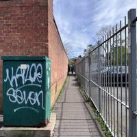 Continue to follow the alleyway with a brick wall on your left and metal fence on the right.