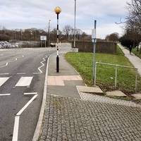 Fork left passing a crossing on the left and then a short, low concrete wall on the right, to reach a roundabout.