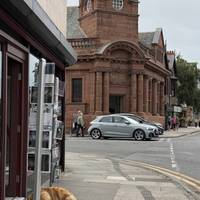 Follow the pavement around the shops towards the tall red brick building.