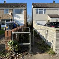 As the road bends by the triangular island, continue straight ahead around staggered barriers onto a footpath between two houses.