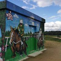 Continue past the attractively painted flood storage building and remain on the higher level path ahead with its sandy surface.