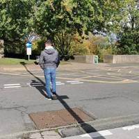 Cross the slightly uneven university access road via the tactile paving. Once over, go right and immediately alongside the low wall.